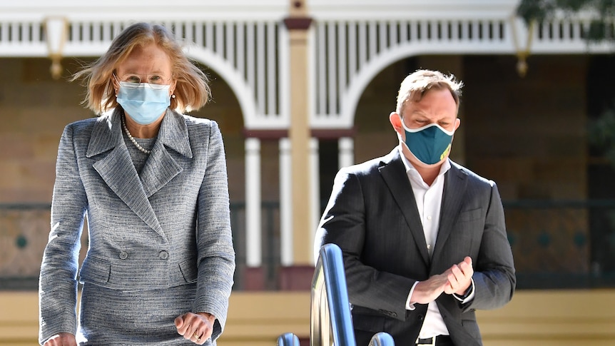 Woman in grey suit and man in dark suit, both wearing masks