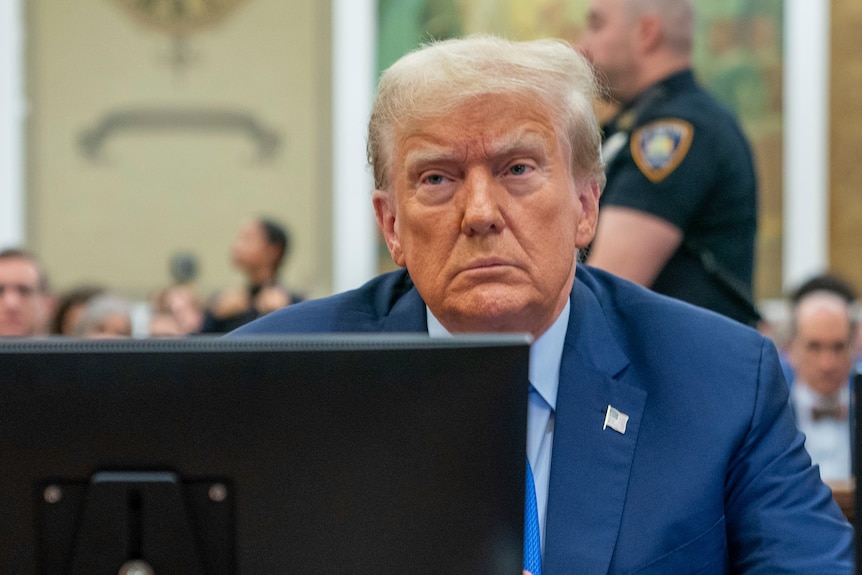 Donald Trump sits behind a laptop in a courtroom. He is frowning.