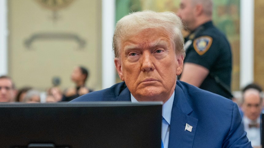 Donald Trump sits behind a laptop in a courtroom. He is frowning.