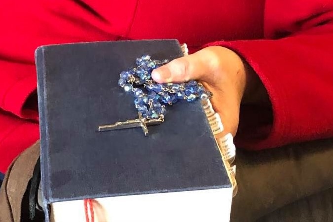 A hand clutches a bible and a bright blue rosary.