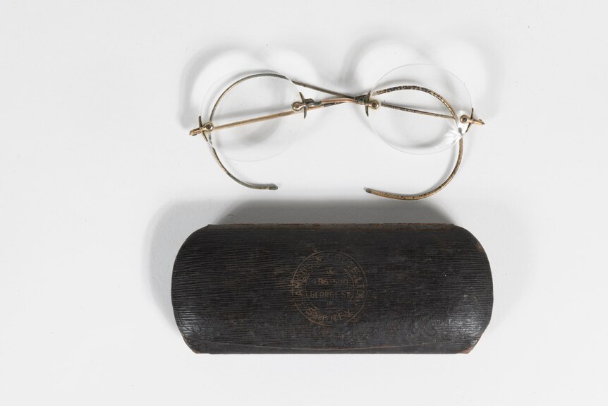 Some gold rimmed glasses without lenses and a black glasses case on a white table.