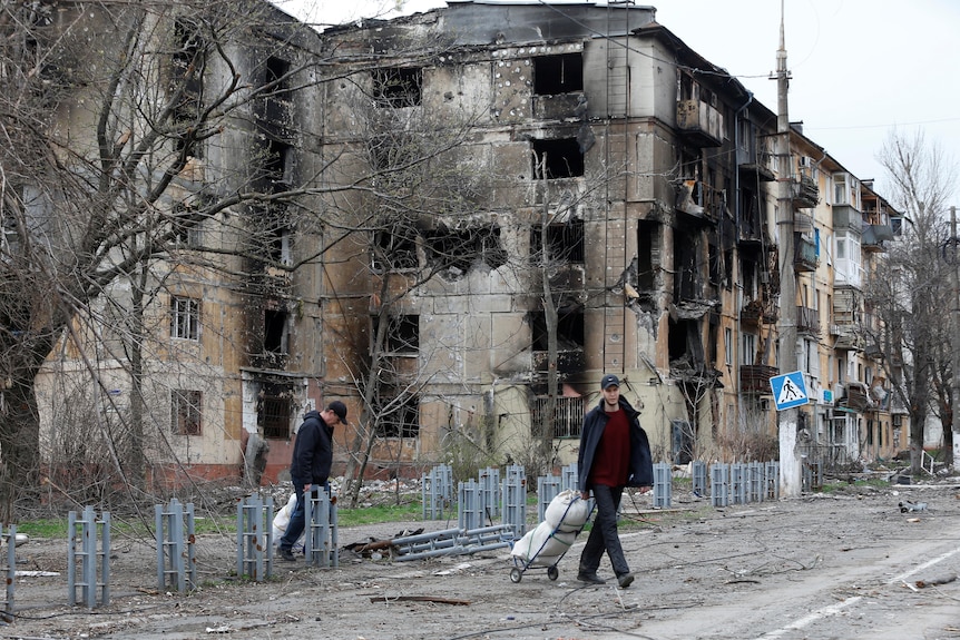 People walk past damaged apartments in Mariupol