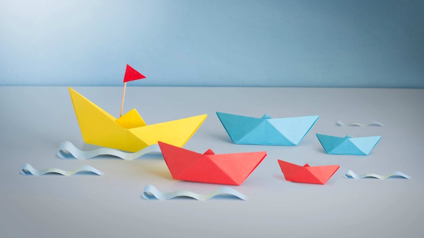 group of origami boats in the ocean being led onwards by a bigger yellow boat with a red flag