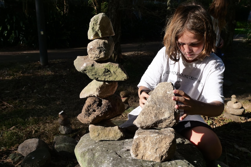 A boy concentrates as he places a rock on top of another one. 