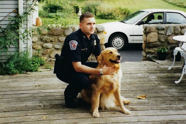 Paul Whelan in uniform, on the front porch of a house, crouched down next to a dog