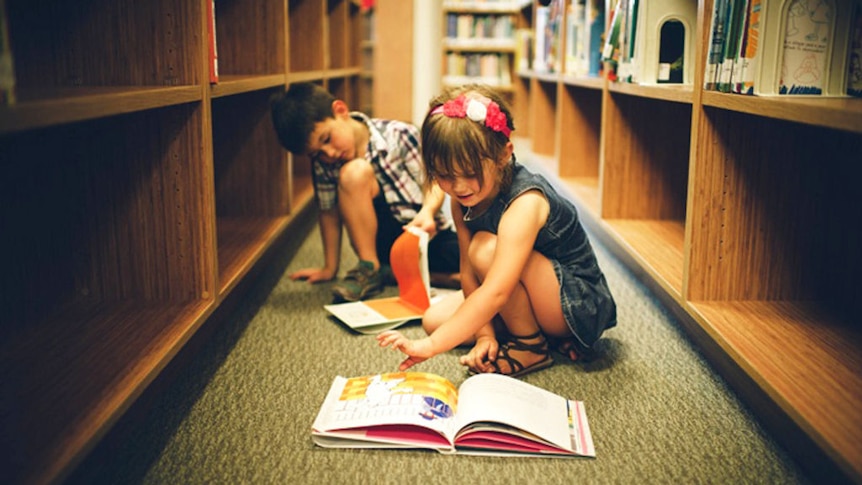 Kids reading books on the ground in a library.