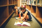 Kids reading books on the ground in a library.