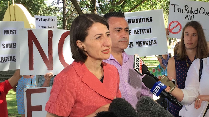 The Premier and Deputy Premier speaking with council merger protesters behind them.