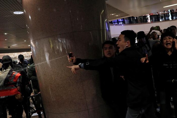 A plainclothes police officer fires pepper spray at a protester with distressed onlookers