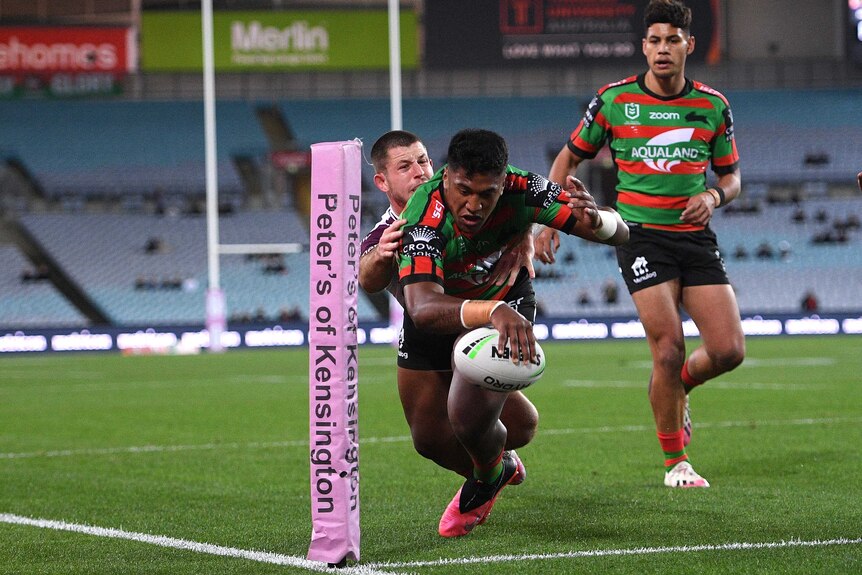 A South Sydney NRL player reaches out with his right hand to ground the ball for a try against Manly.