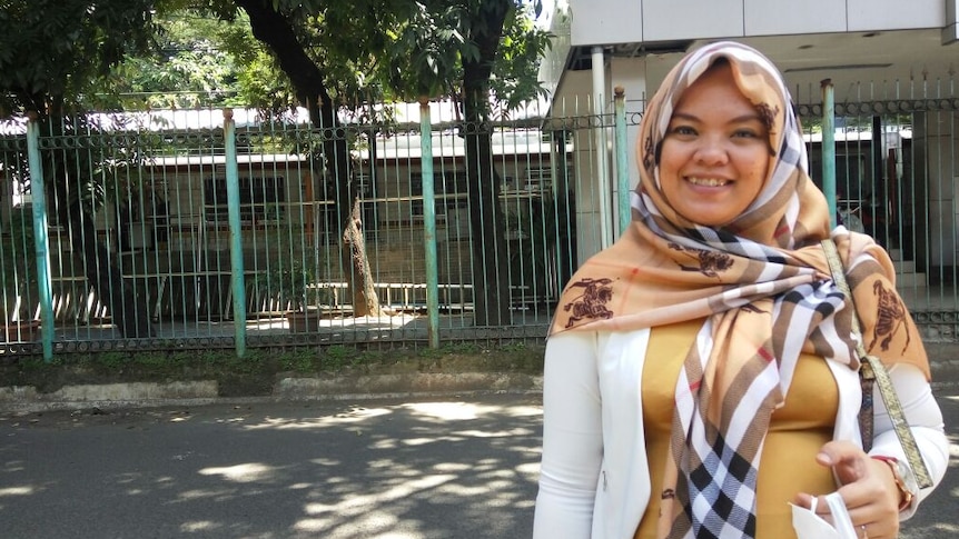 Siti Wahyuni is standing on the sidewalk.