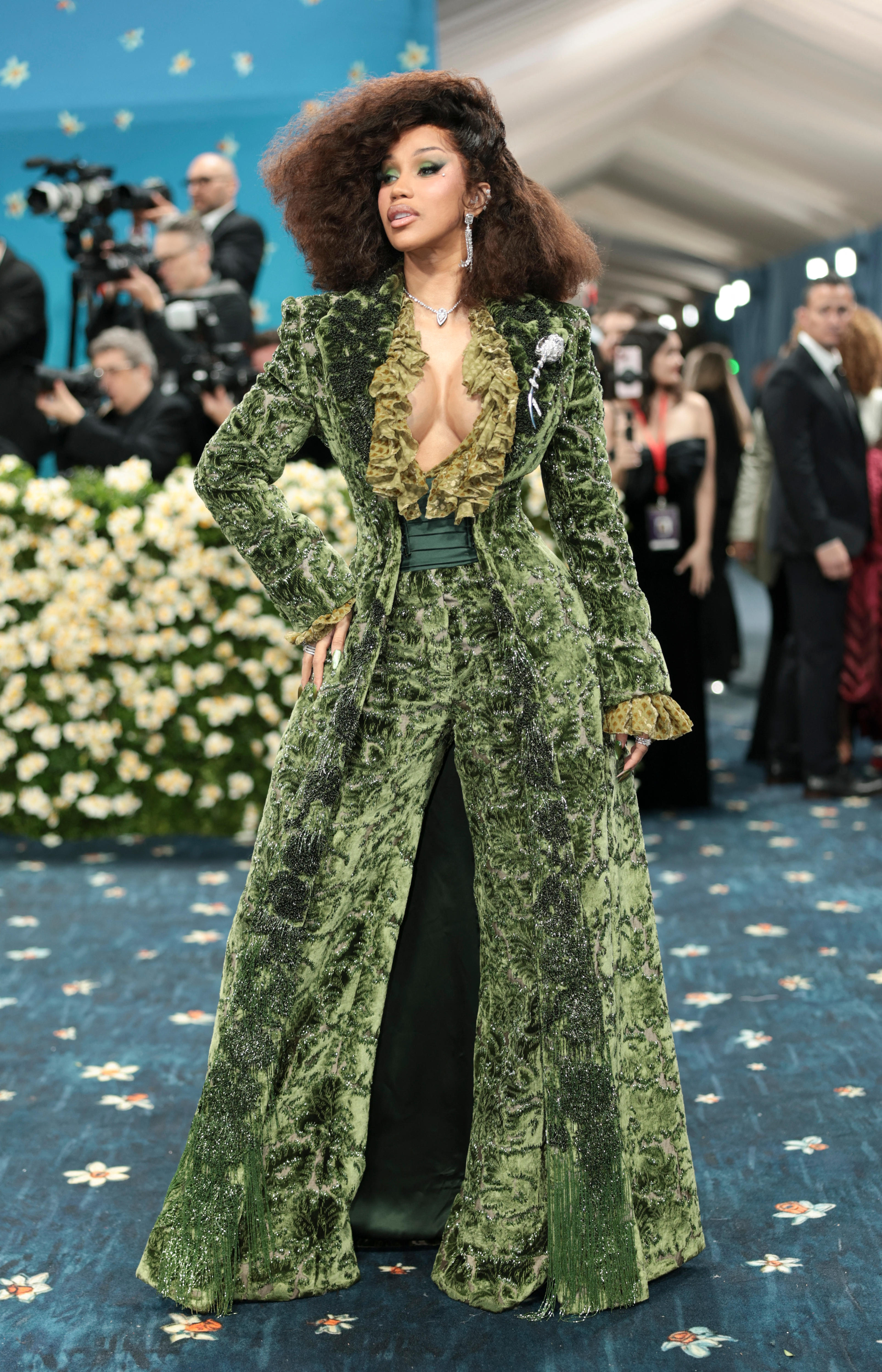 Cardi B wearing a long green velvet pantsuit with a light green ruffled plunging neckline and a silky sash