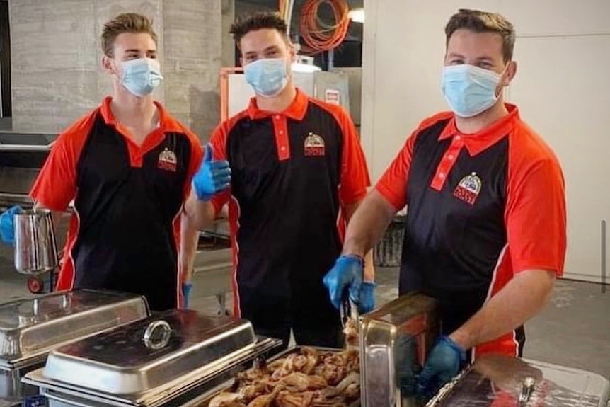 Three men in masks serving food from bain-maries at a function