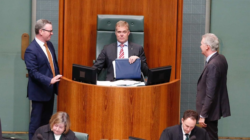 Tony Smith sits in the Speaker's chair, raising one eyebrow. Christopher Pyne and Tony Burke stand on each side of him