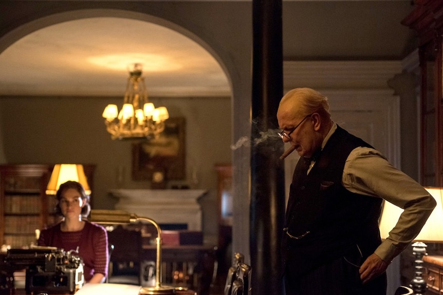 A scene from Darkest Hour where Winston Churchill smokes a cigar in his office while a secretary watches on.
