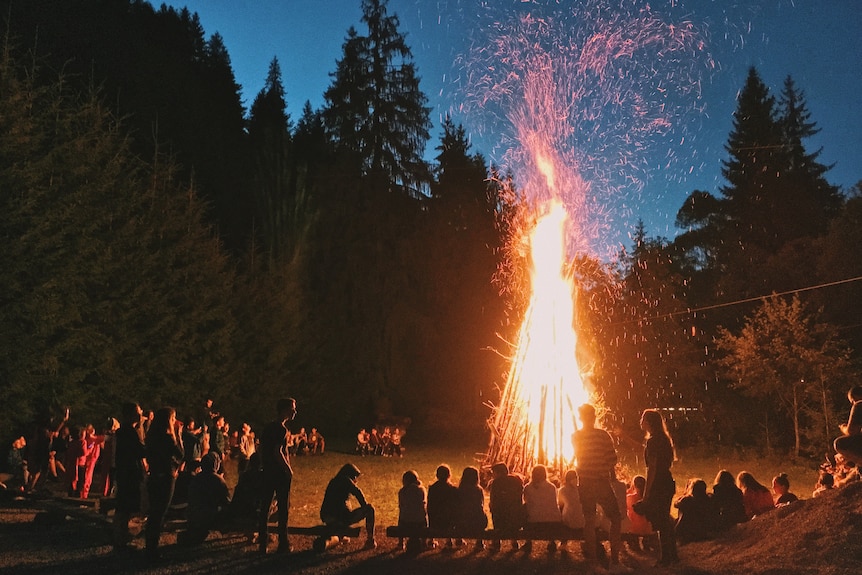 A burning bonfire in a forest surrounded by a group of people