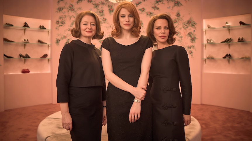 Three women in a black dresses, coiffed hair, early 60s period costume/setting, in a department store