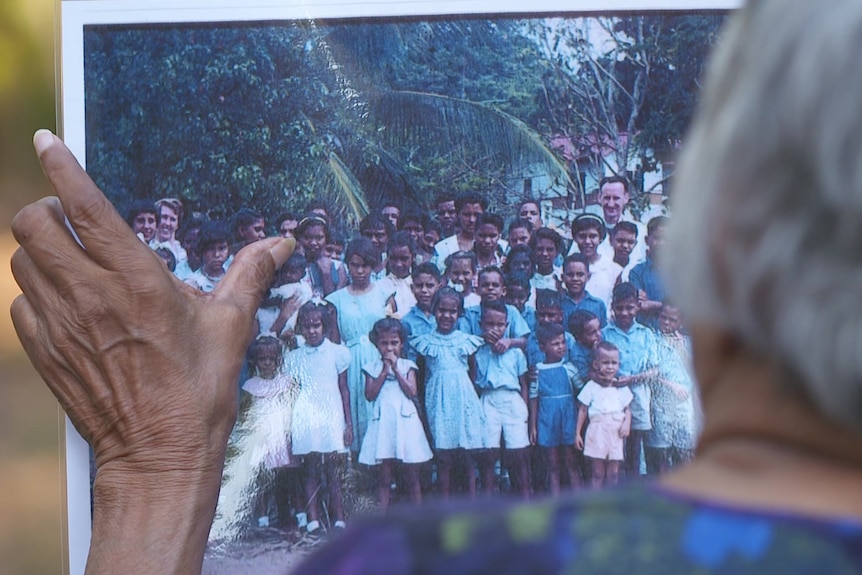 Elderly Indigenous woman looking at a large photo.