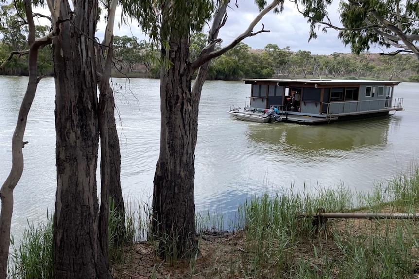 a houseboat on the river with trees in the foreground