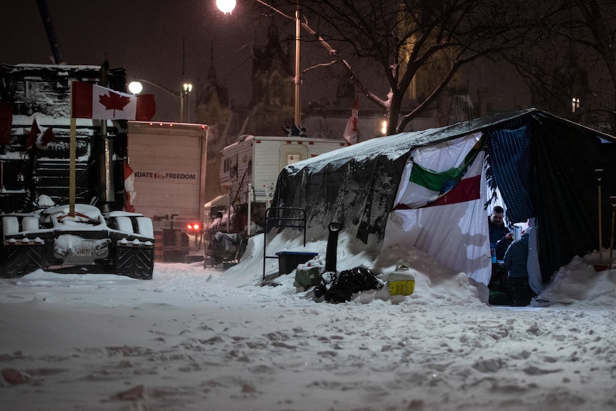 A tent is set up next two a prime mover with a Canadian flag attached to it. A heavy layer of snow blankets the ground.