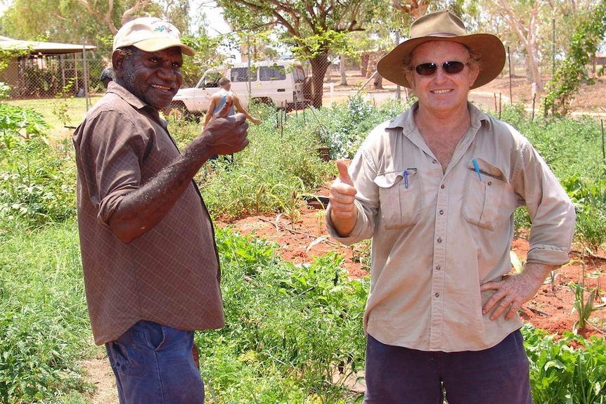 Two men with thumbs up in a garden.