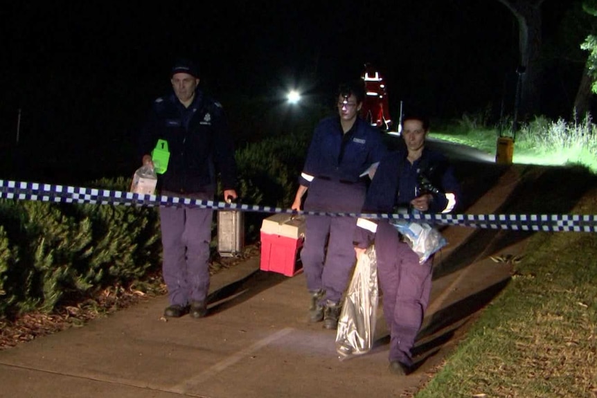 Detectives carry evidence out of an alleged crime scene at night.