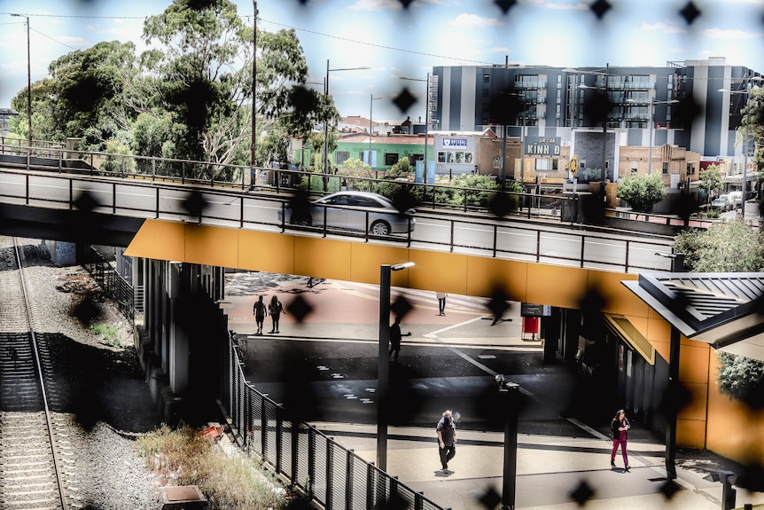 People are seen walking on a foorpath through the palings of a fence