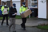 Two male British police officers, one man in dark sweater and cap hold boxes and clipboards