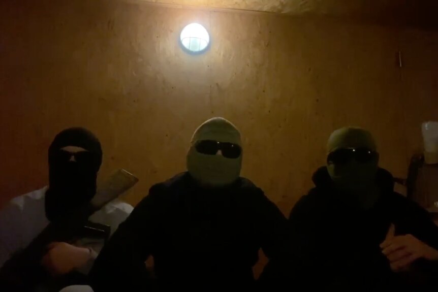 Three people wearing head covers and sunglasses sit in a dimly lit room