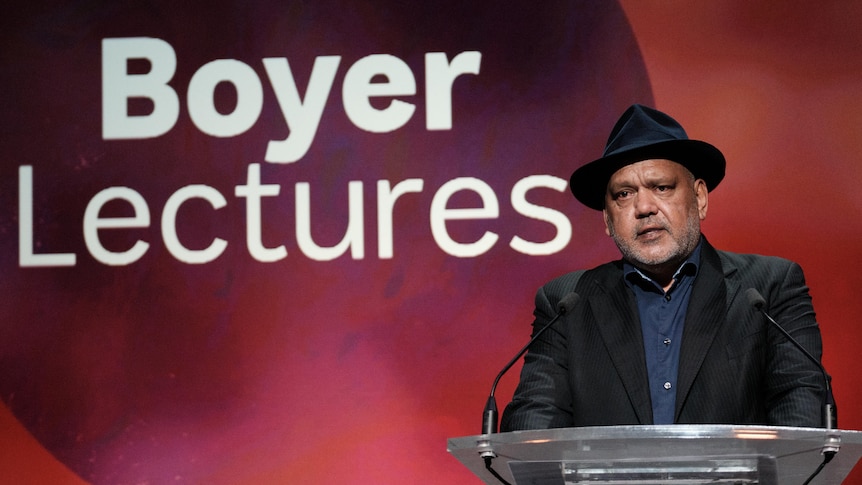 An Aboriginal ,man in a black suit standing at a lectern