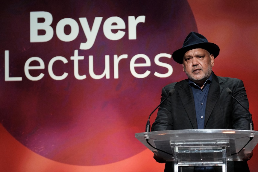 An Aboriginal ,man in a black suit standing at a lectern