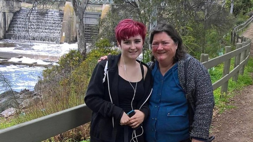 woman and daughter, standing and smiling near a water feature
