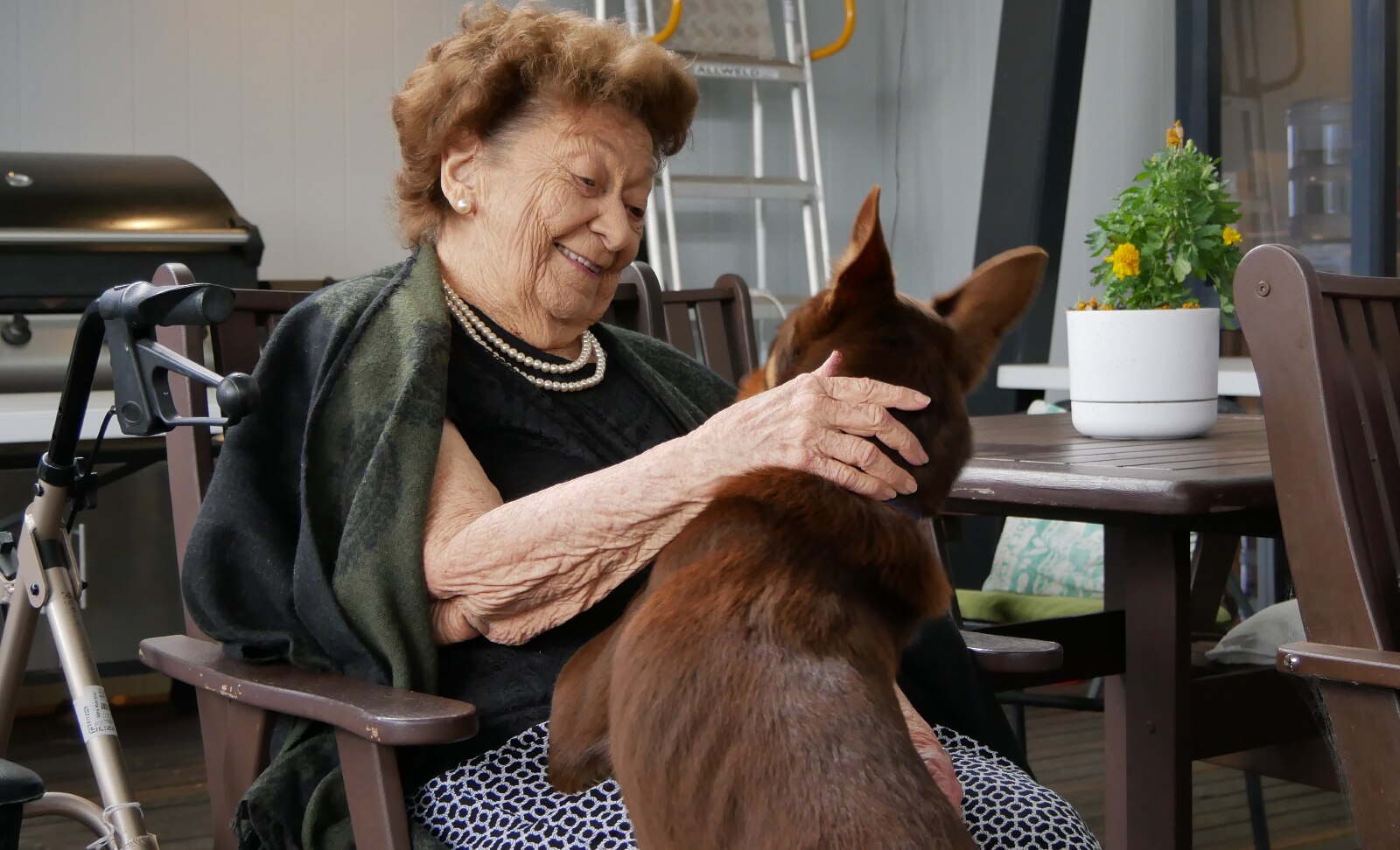 Merle, an older woman, sitting in a chair with her hand resting on a dogs back, dog has both paws on woman.