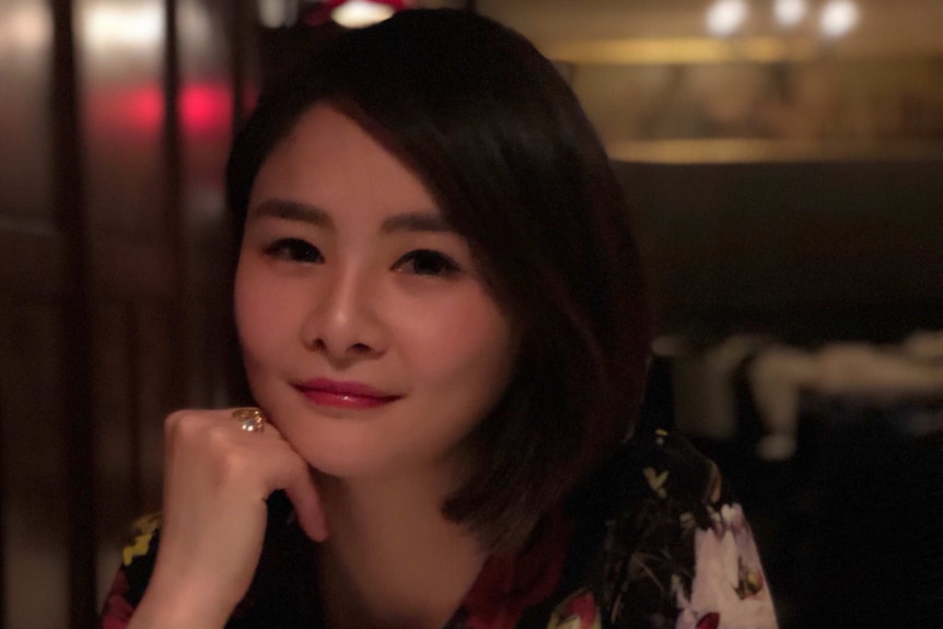 A woman sits in front of a table with her right hand holding her chin.