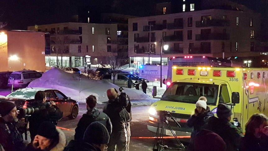 An ambulance with flashing lights and news reports at the shooting scene.