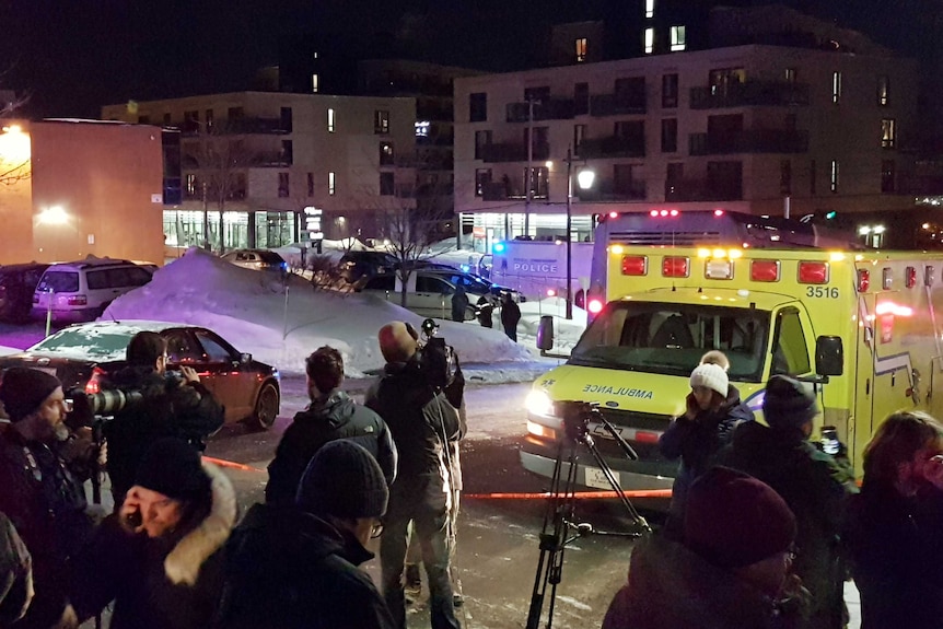 An ambulance with flashing lights and news reports at the shooting scene.