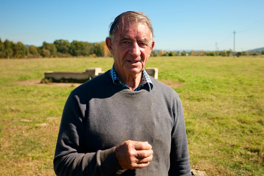 A man with grey hair stands in a pasture looking serious.