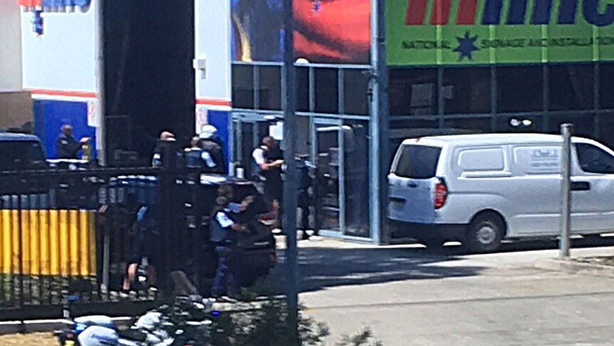 Photo from across the street of heavily armed police surrounding Inline National Signage, the location of the siege.