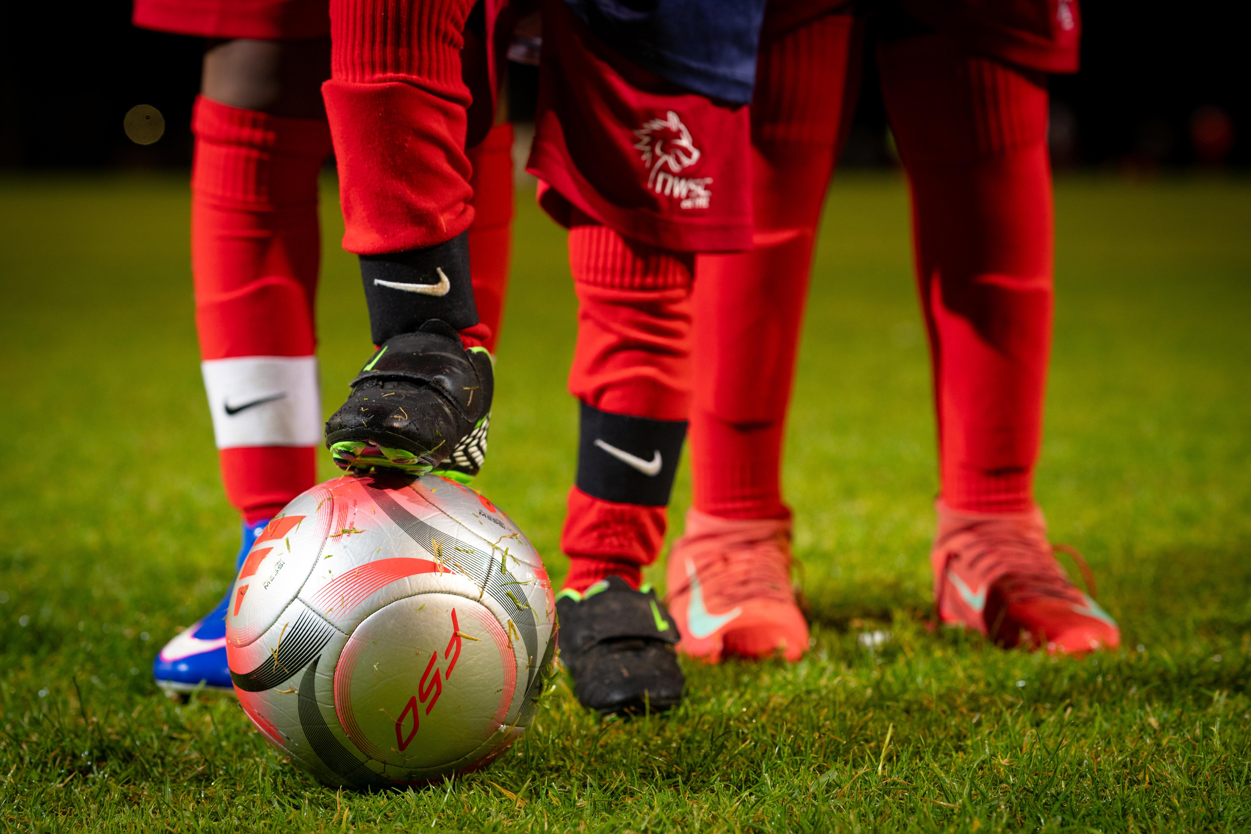Three pairs of legs wearing long red soccer socks, one of which is resting on a soccer ball