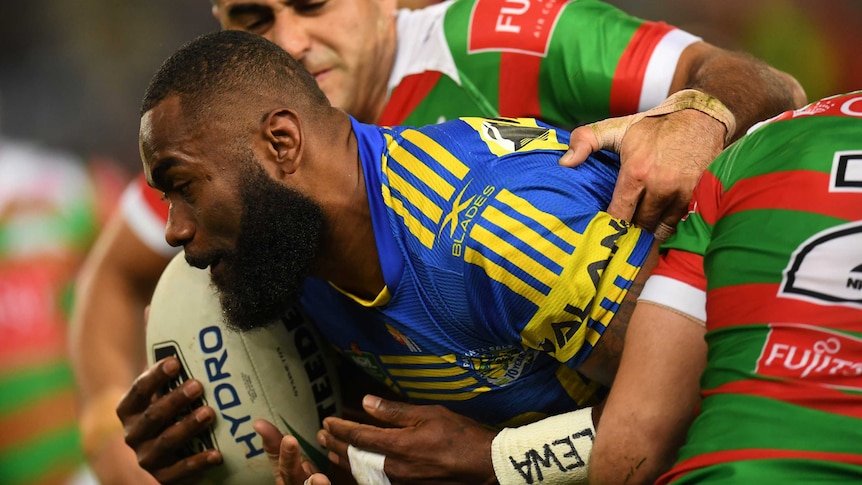 Semi Radradra holding the ball as he is tackled by South Sydney players.