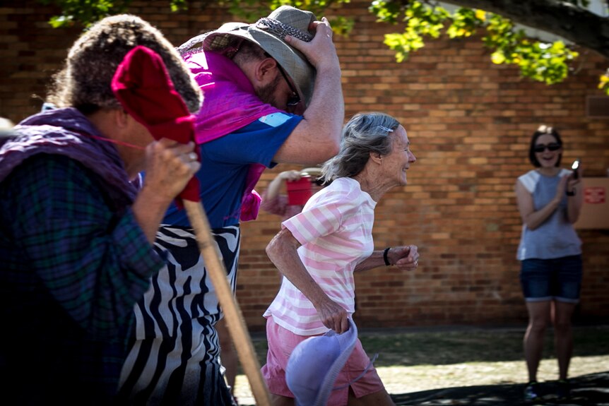 Three people racing down the street dressed in old women's clothes.
