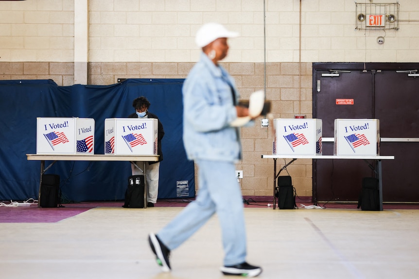 A person walks past a row of boxes labelled with an American flag and "I voted".
