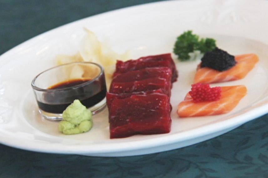 A white dinner plate with red whale meat and garnishes sits on a table.