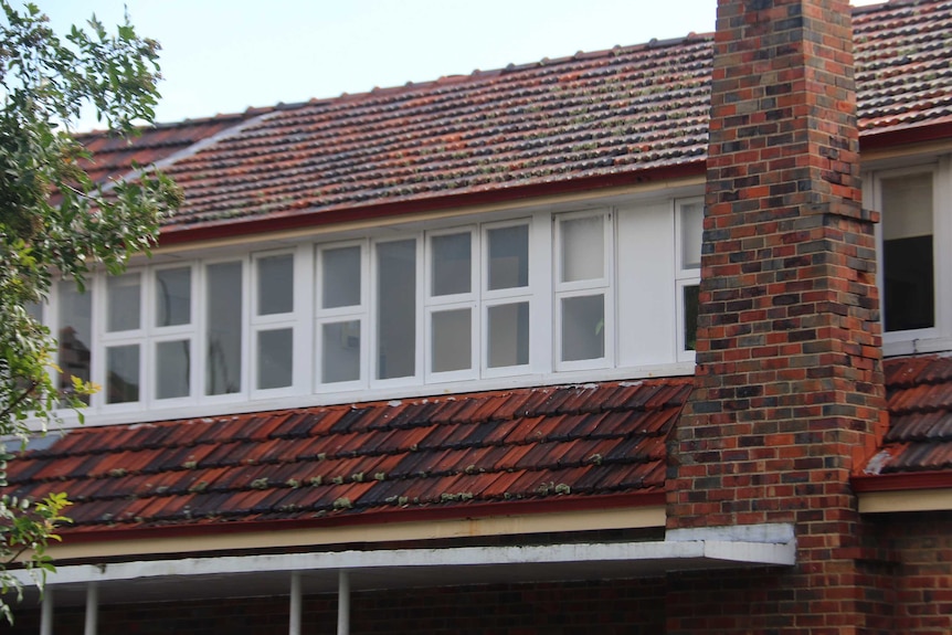 A row of white frame windows line the second storey of the red brick Warinda Hostel.