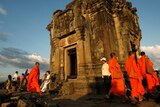 monks and tourists walks around a building at angkor wat