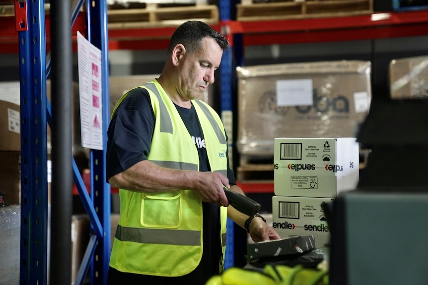 A man in yellow high-vis vest scans a parcel.