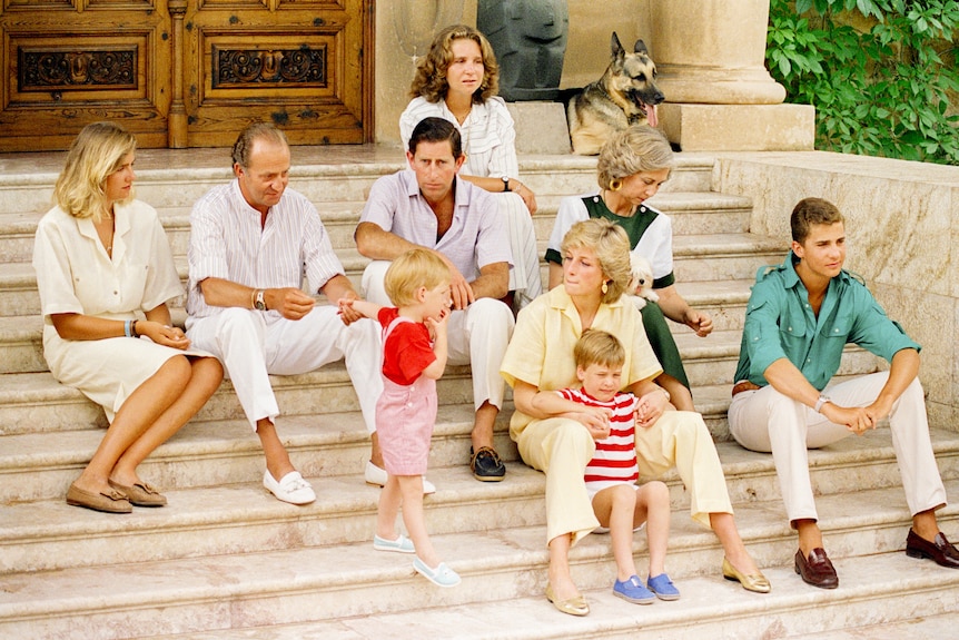 A group of men, women and children sit together on the steps of a large home