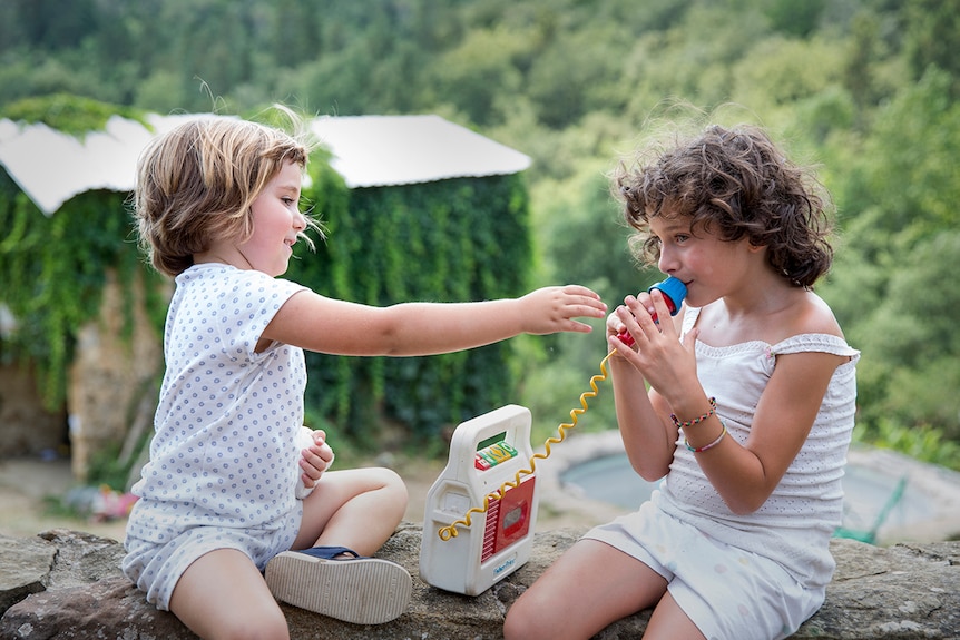 Colour photo from 2017 film Summer 1993 of child actors Paula Robles and Laia Artigas playing outside with a toy microphone.