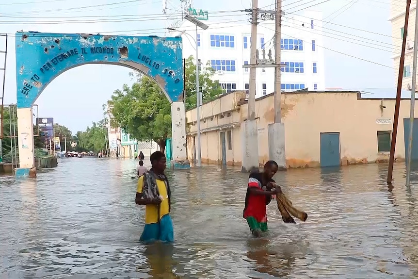 A wide photo of two men walking through a flooded street in Somalia, with a large archway behind them going over the road.