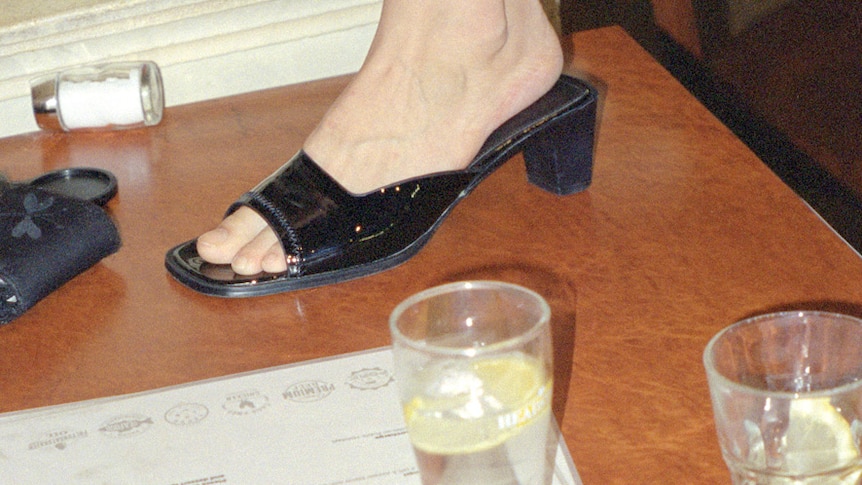 Book cover with a picture of a woman's foot in an open black heel on a lino floor, next to two glasses with a lemon slice inside